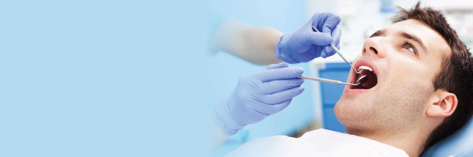 A man sitting on a dentist chair, with his mouth open and his teeth visible